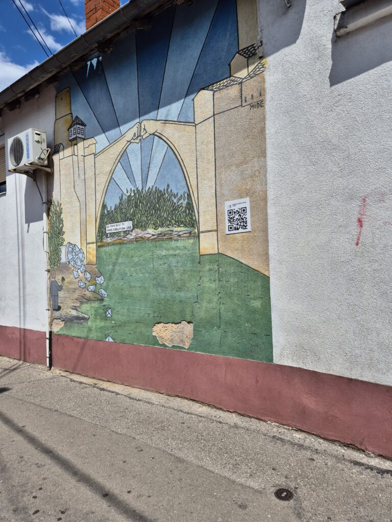 Mural na ścianie kamienicy przedstawiający dwie części łuku Starego Mostu w Mostarze, które stykają się, zbijając "żółwika".
